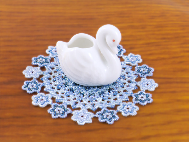A swan ornament is put on the blue flower doily.